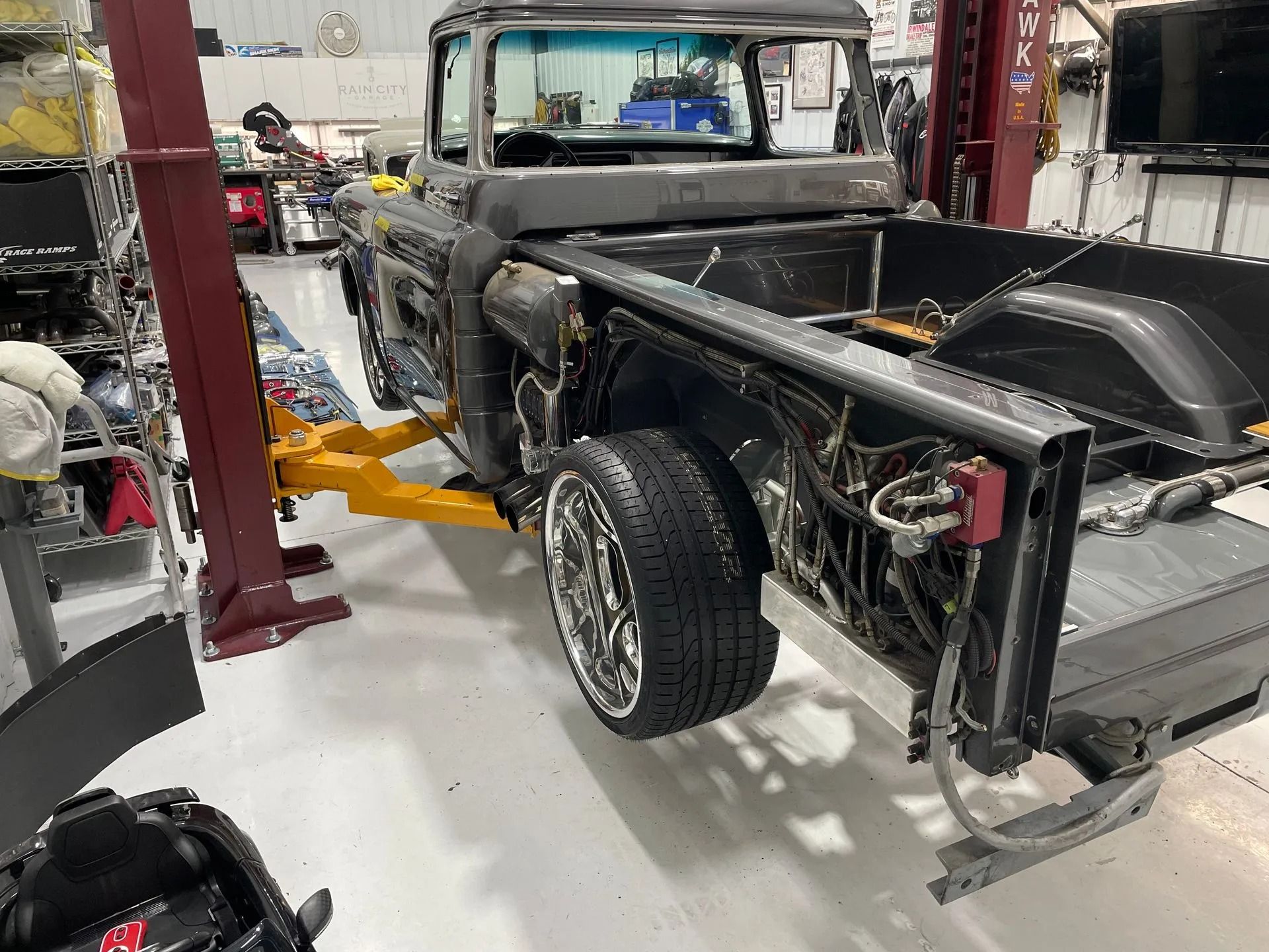 Classic black pickup truck in a repair shop, raised on a lift with rear wheels removed.