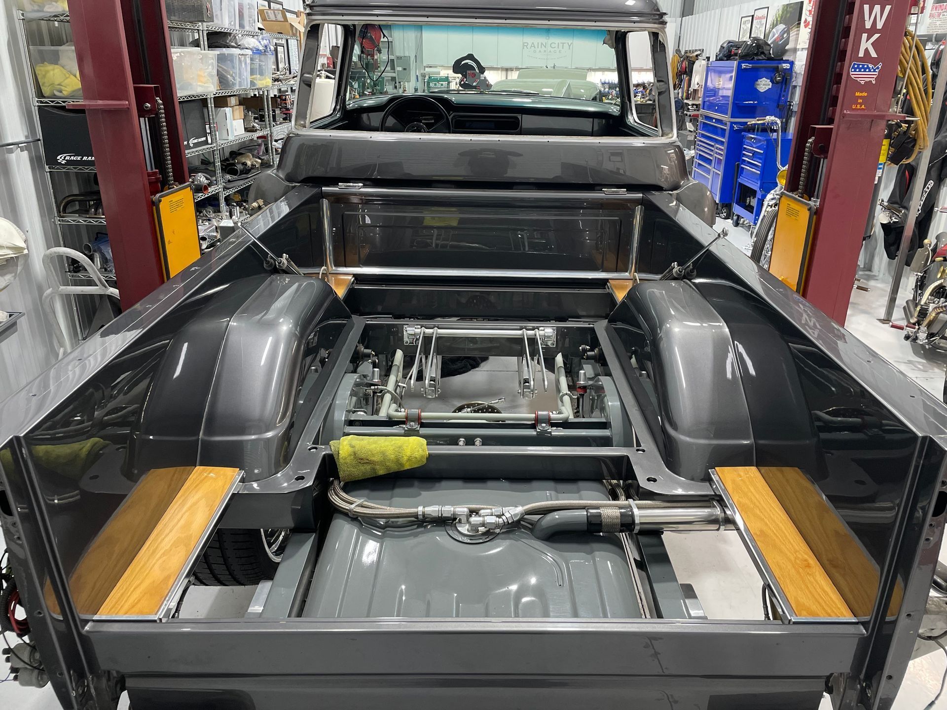 Vehicle chassis in an auto shop with exposed frame, black body panels, and tools inside the bed area.