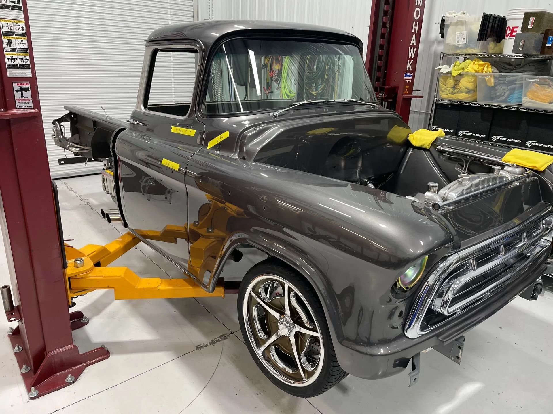 Classic black pickup truck on a lift in an auto garage, with yellow support arms attached.