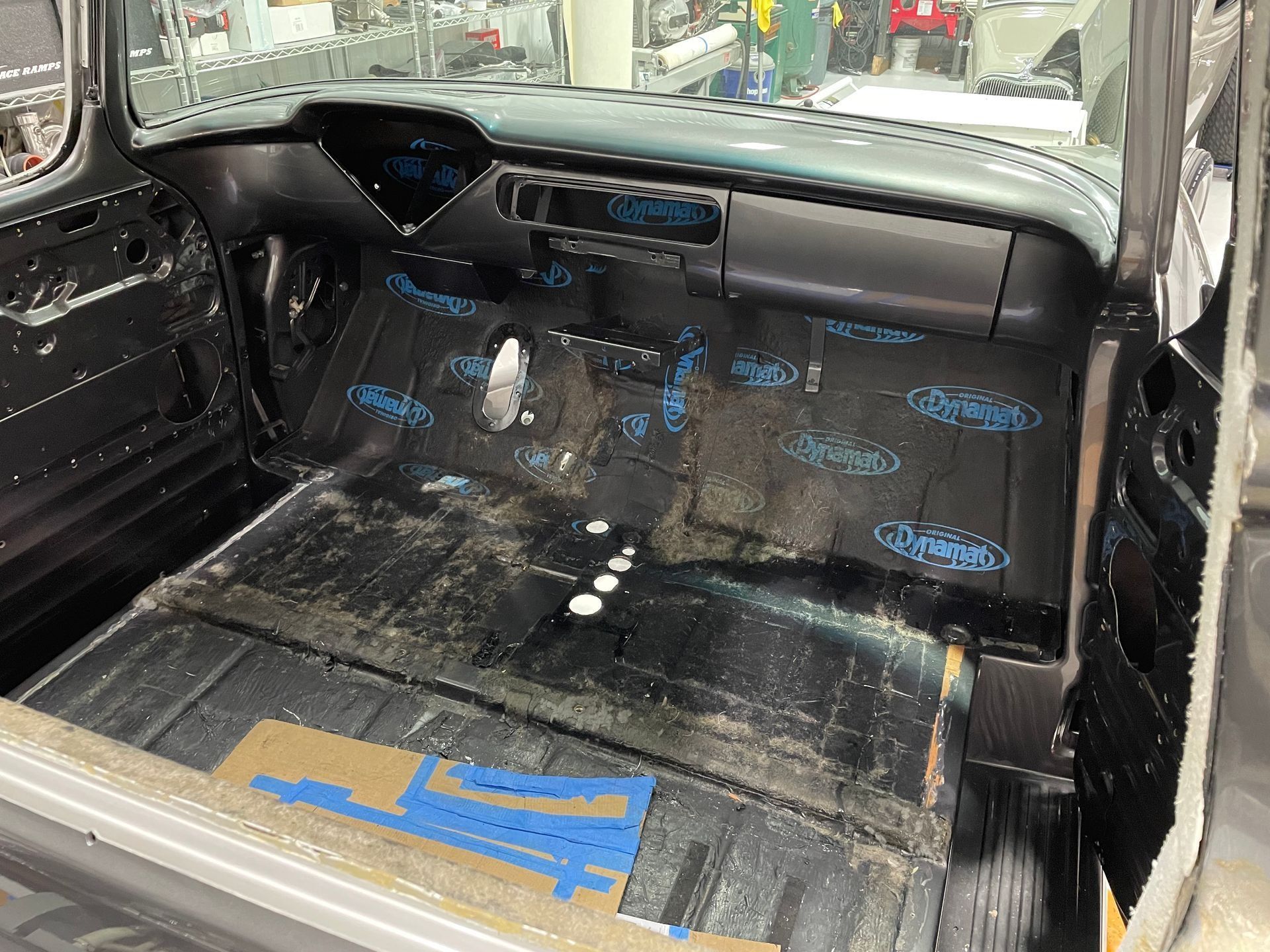 Empty car interior with black flooring, blue tape markings, and the dashboard visible