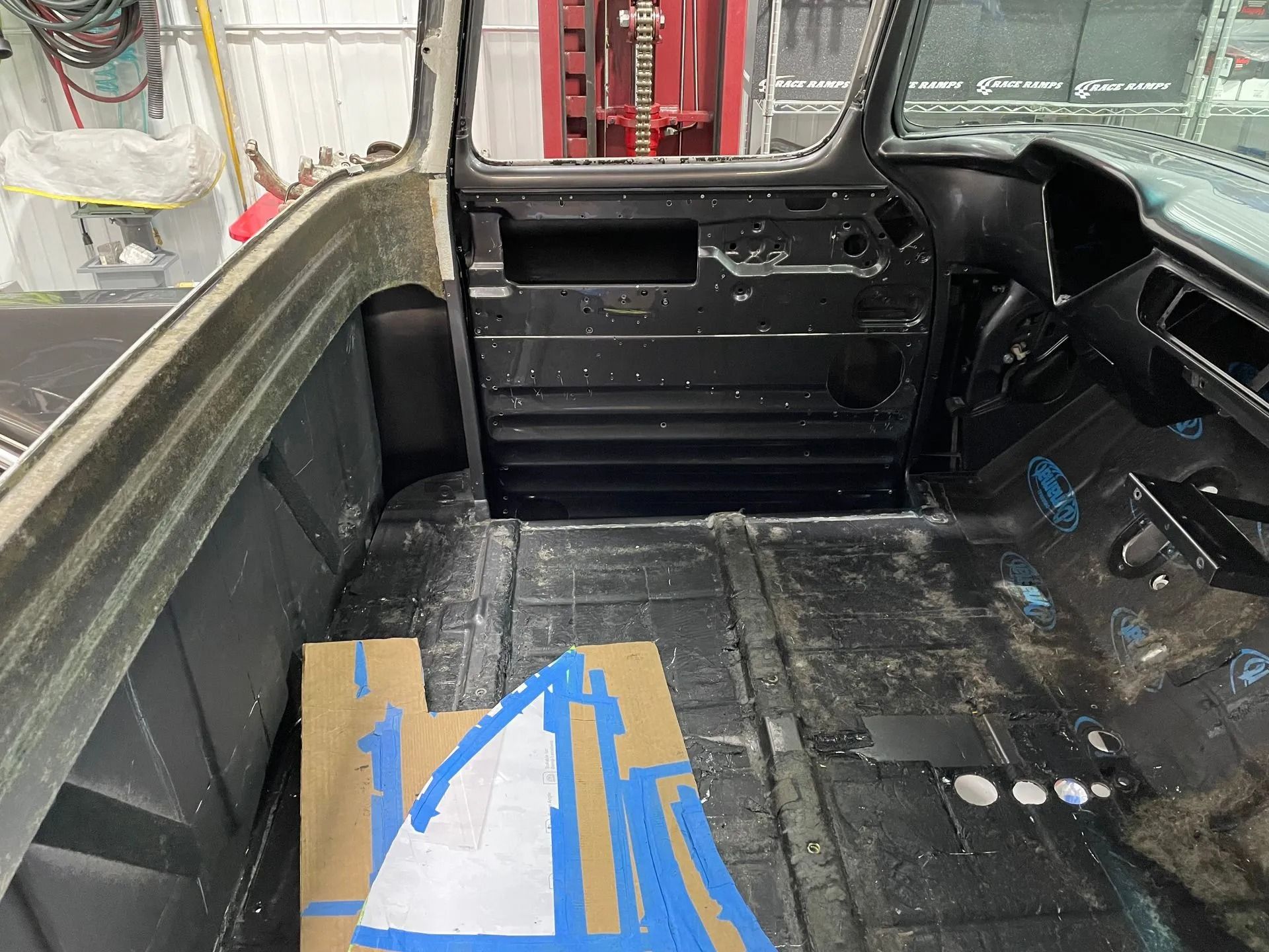 Truck bed interior with black liner and a cardboard sheet taped to the floor.
