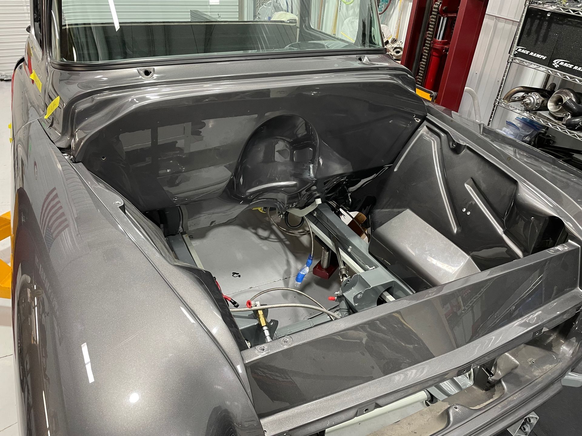 Silver car with exposed rear engine bay and trunk area in a workshop.