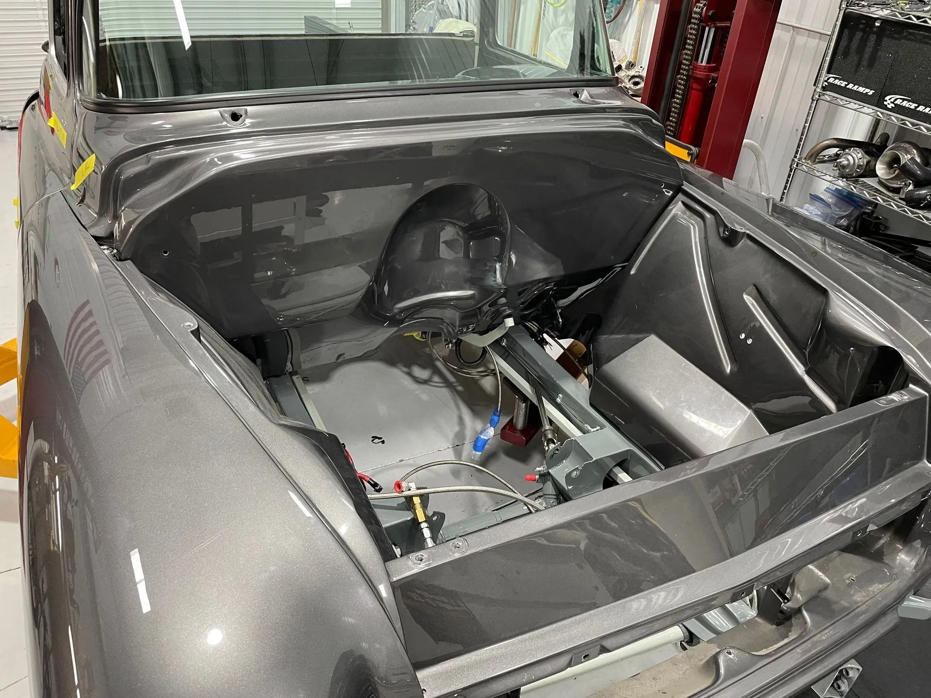 Gray car with exposed rear engine bay and open bodywork in a garage