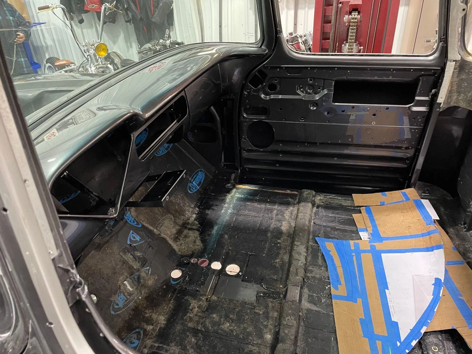 Car interior stripped to bare metal with blue tape marks on the floor and passenger side panel removed