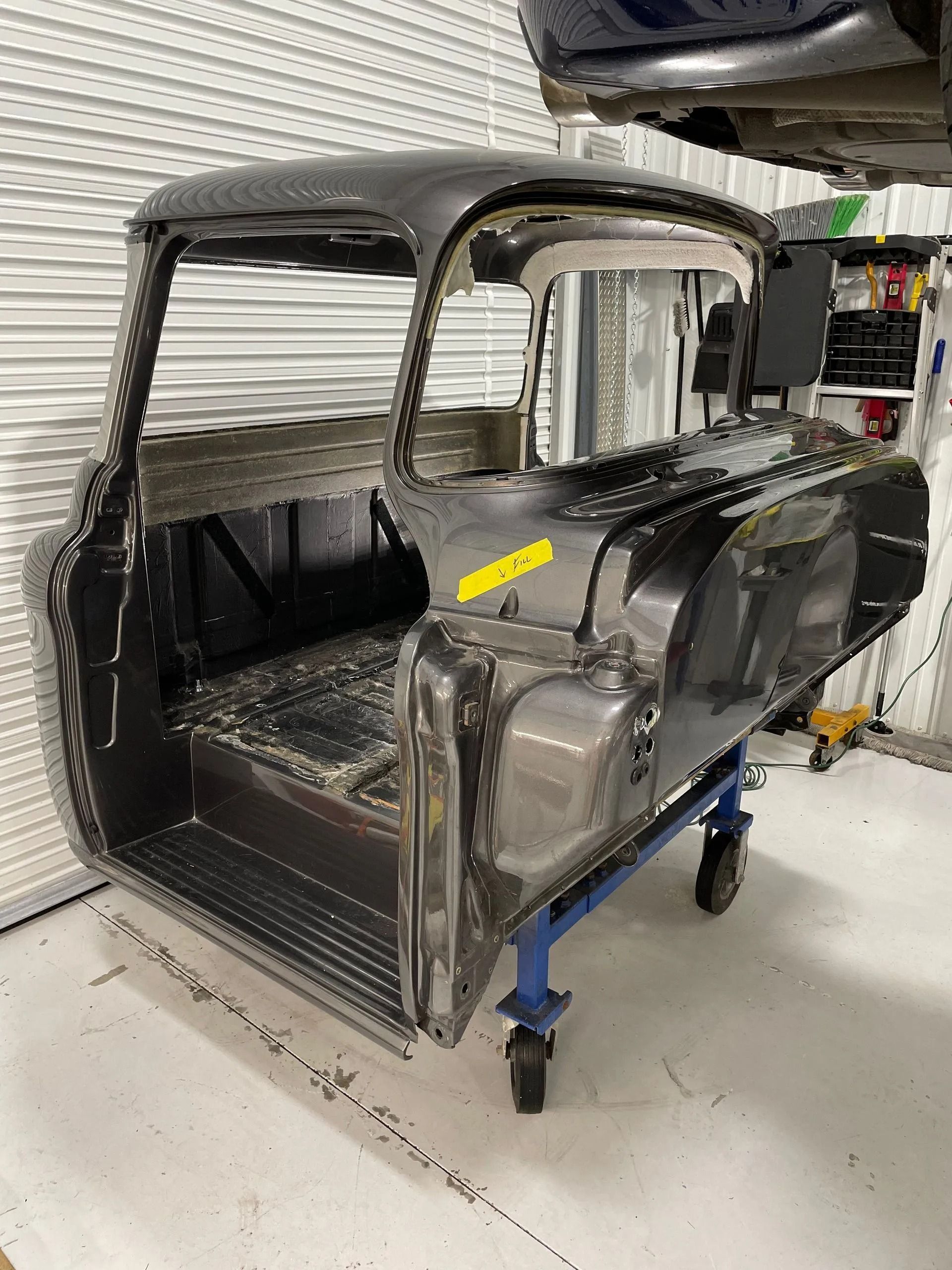 Partially restored black vintage car body in a workshop, with primer patches and blue support stands