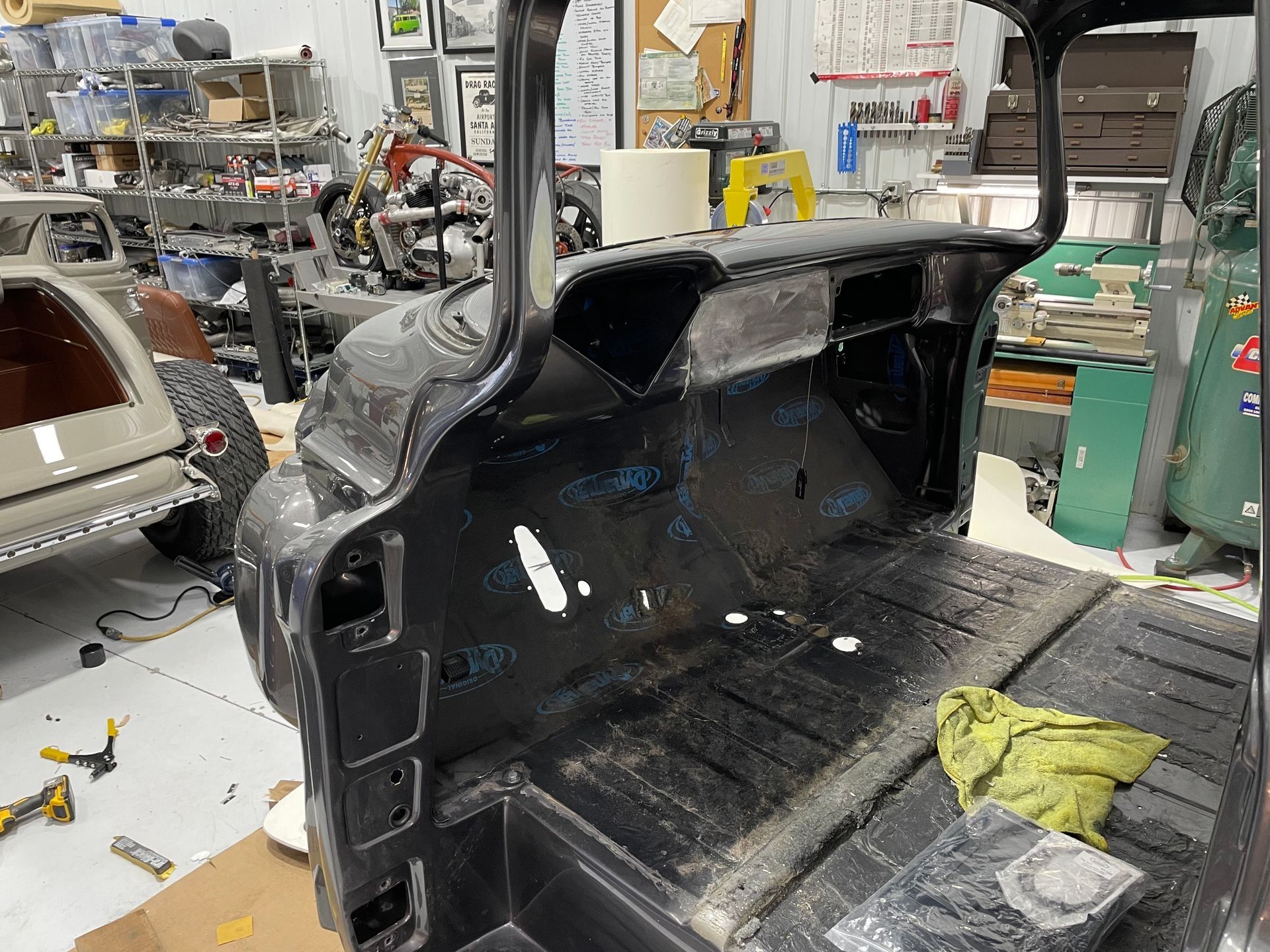 Black car trunk interior in a garage, with exposed metal and tools nearby during repair.