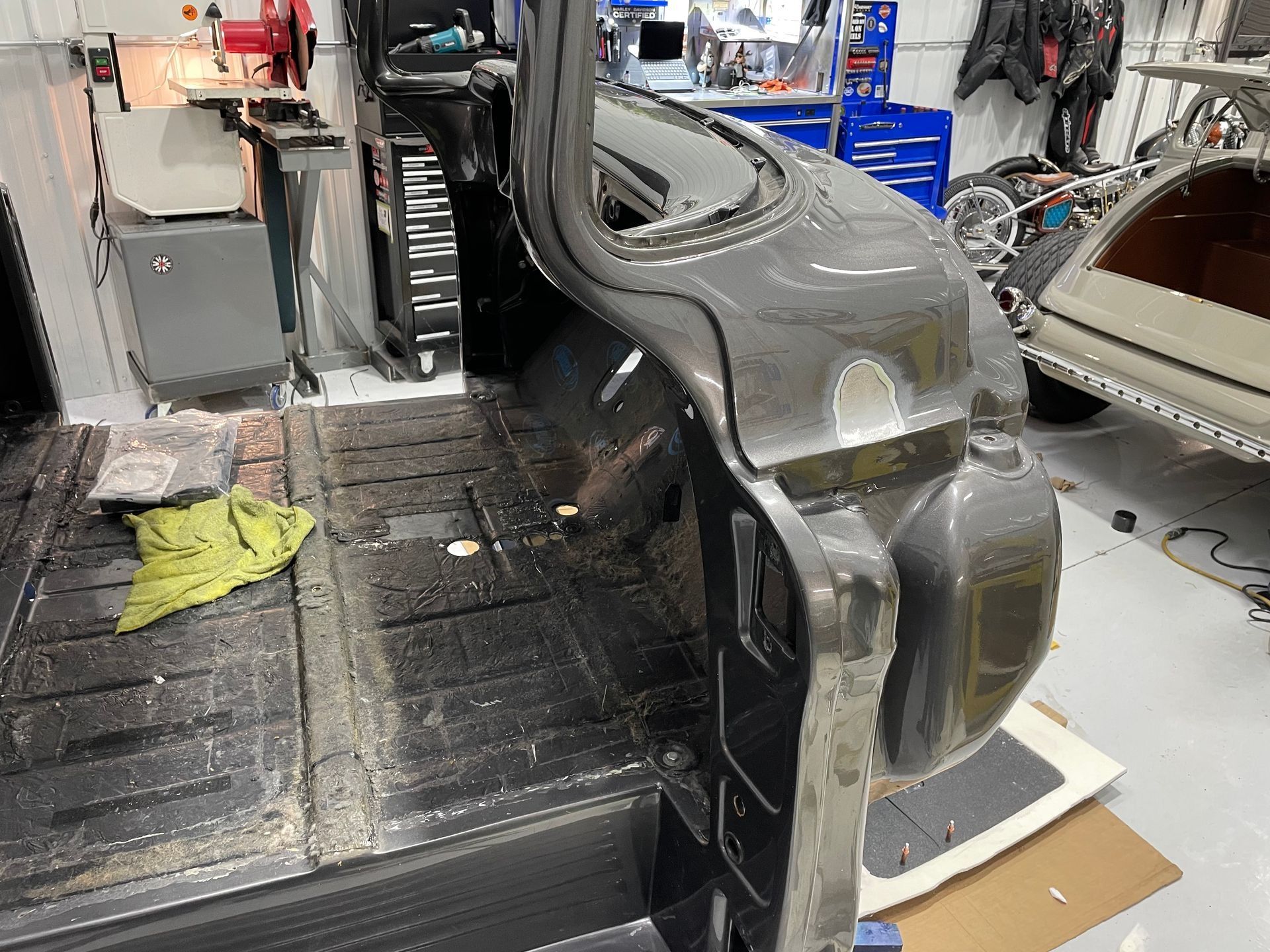 Gray car body shell in an auto repair shop, with tools, parts, and a workbench nearby.