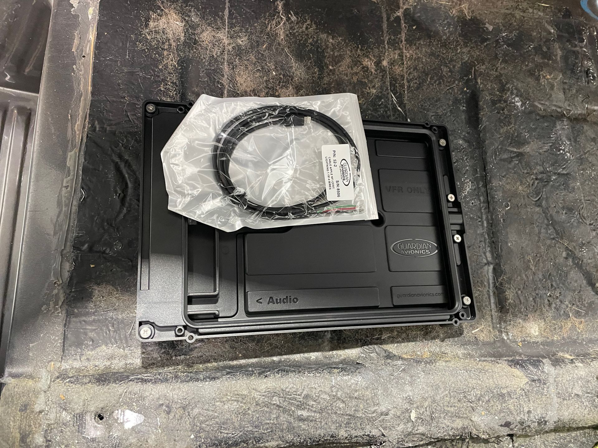 Black device in a concrete recess, partly covered with plastic-wrapped cable and lying on a tray.