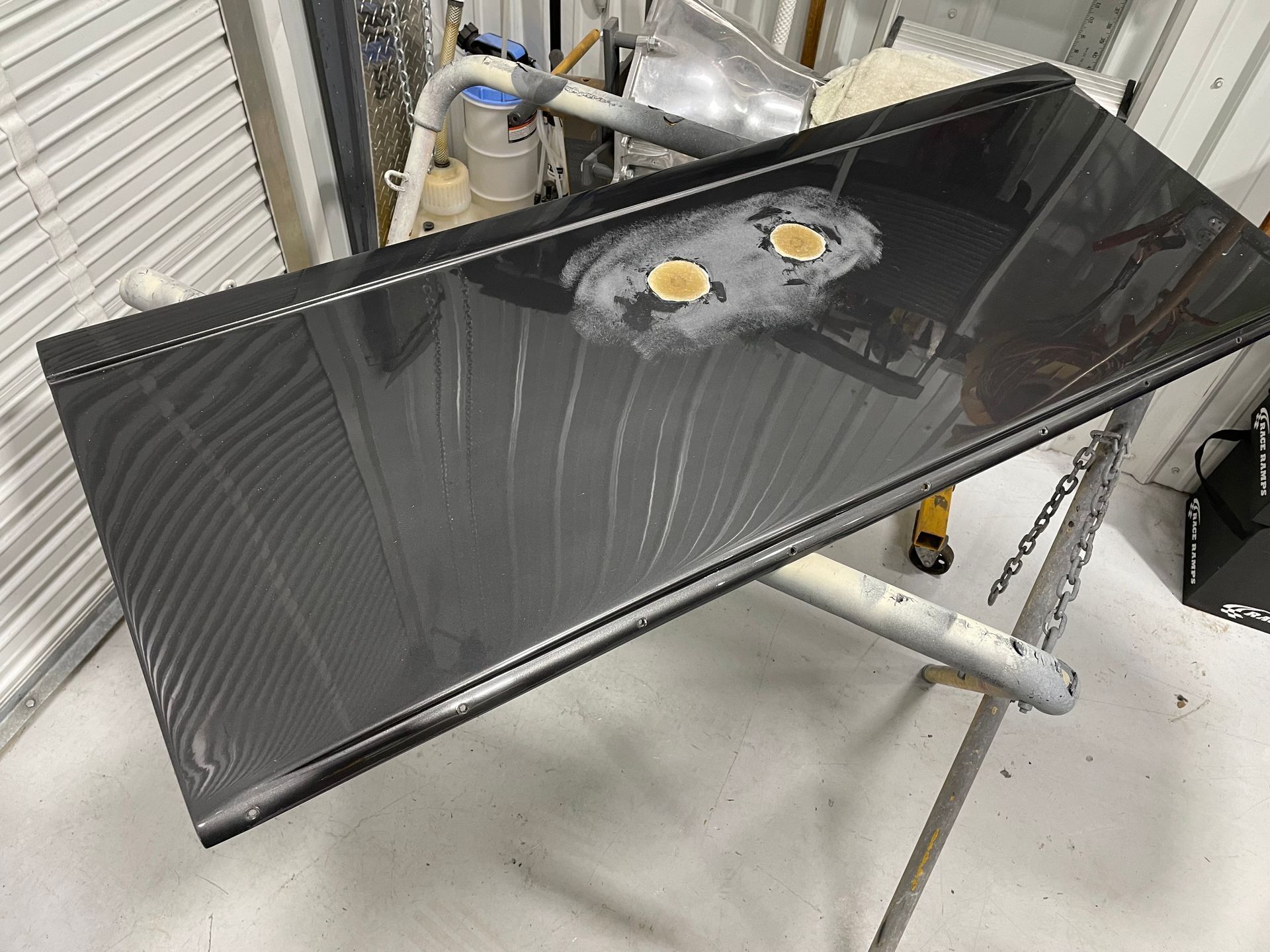 Glossy black rectangular panel on a metal stand in a workshop, with two circular cutouts near the top.