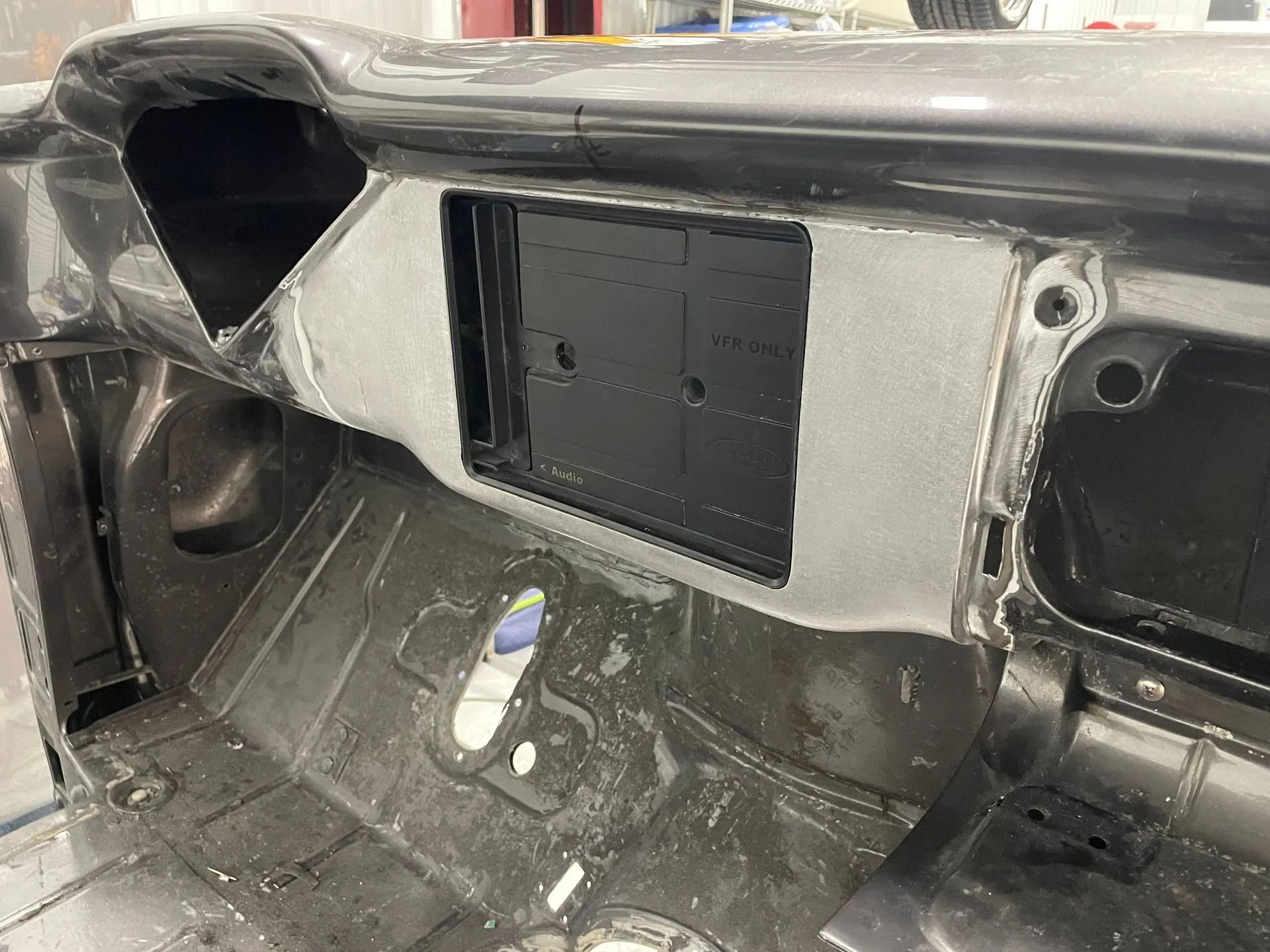 Close-up of a stripped car interior dashboard area with black and gray panels and exposed components