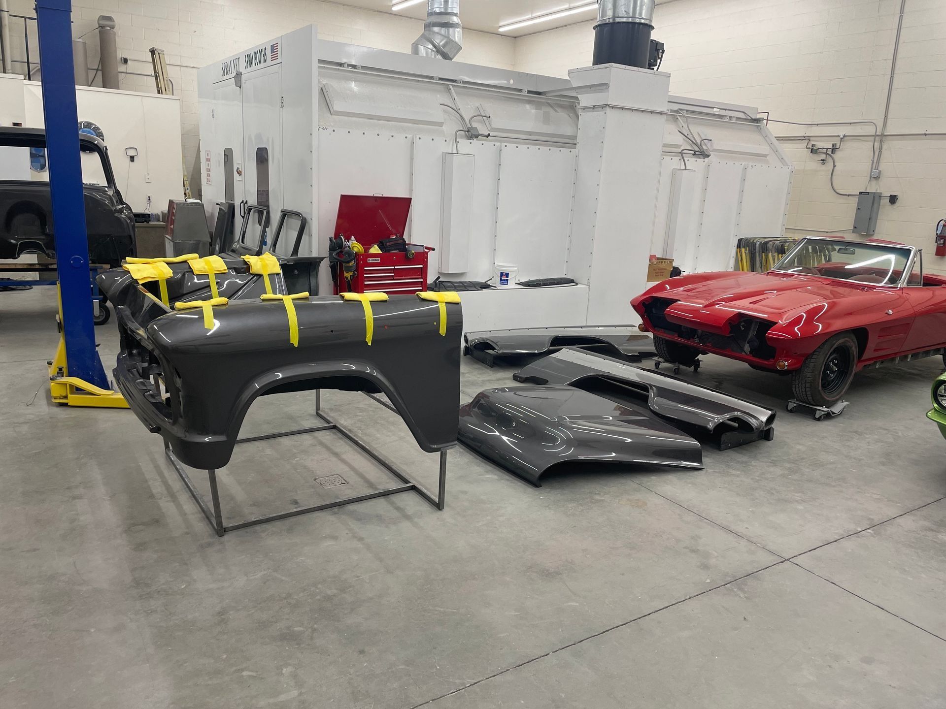 Classic car restoration shop with red convertible, black car parts, and a body panel on the floor