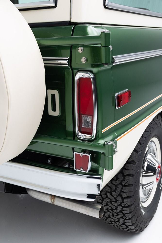 Rear corner of a green vintage SUV with white roof, spare tire, taillight, and off-road tire visible