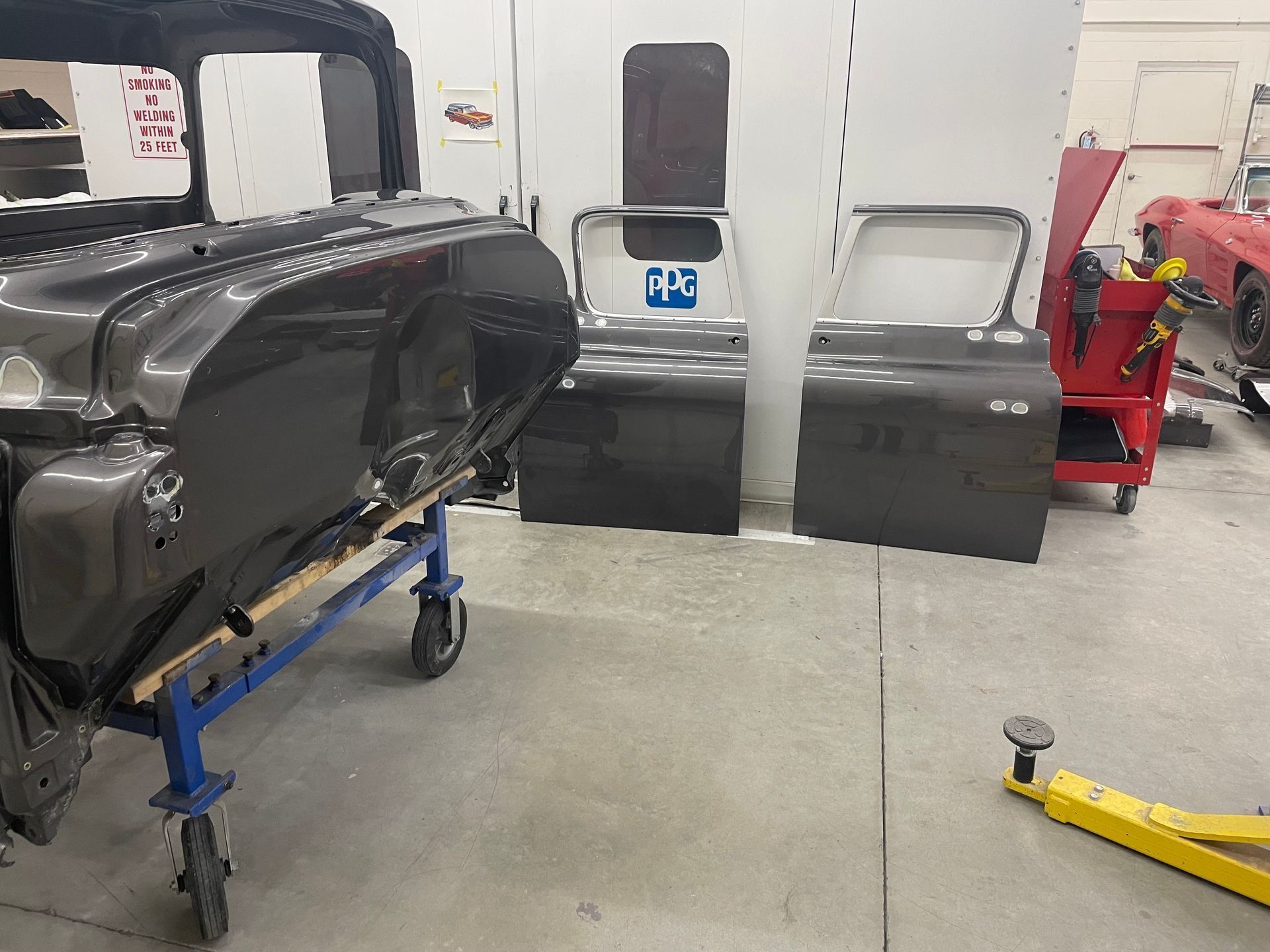 Auto body shop with a black car body on a blue stand and car doors leaning against the wall.