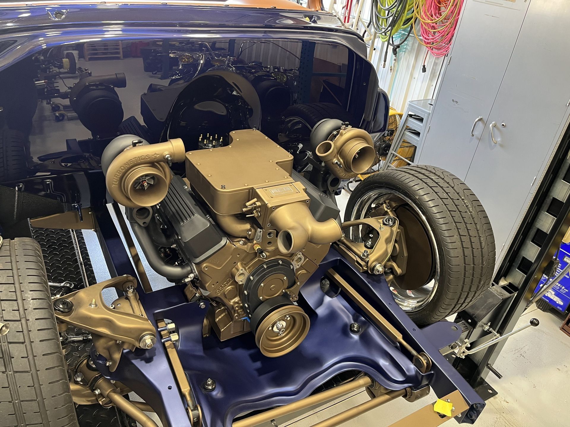 Car chassis with exposed engine and suspension parts in a workshop, shown on a blue frame.