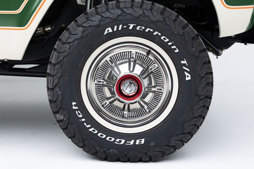 Close-up of a black off-road tire with chrome wheel on a green-and-white vehicle