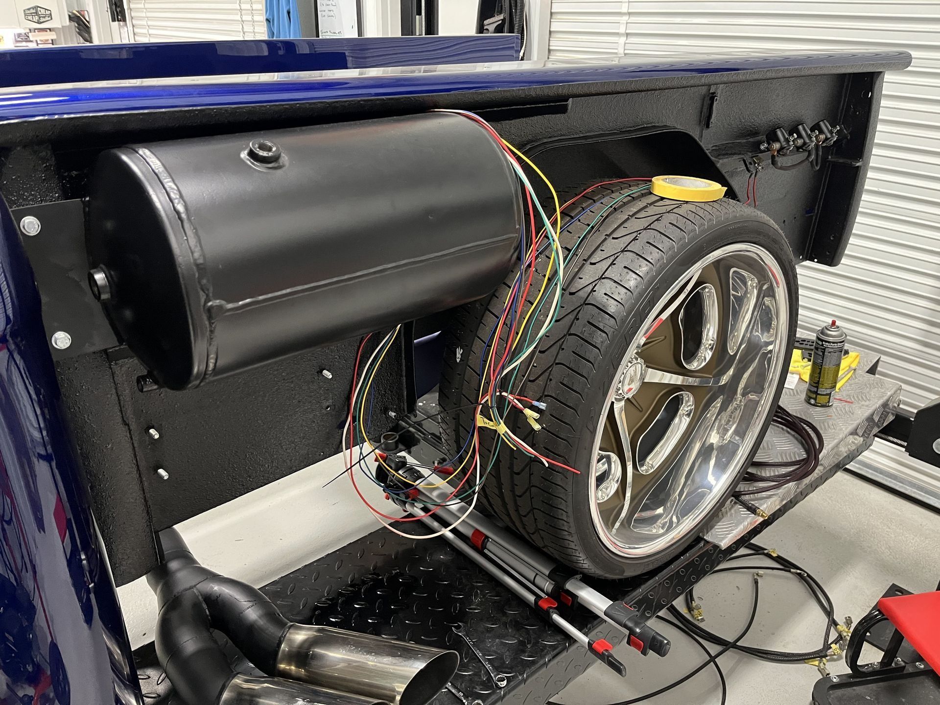 Open truck bed with exposed tire, wires, and black cylindrical tank inside.
