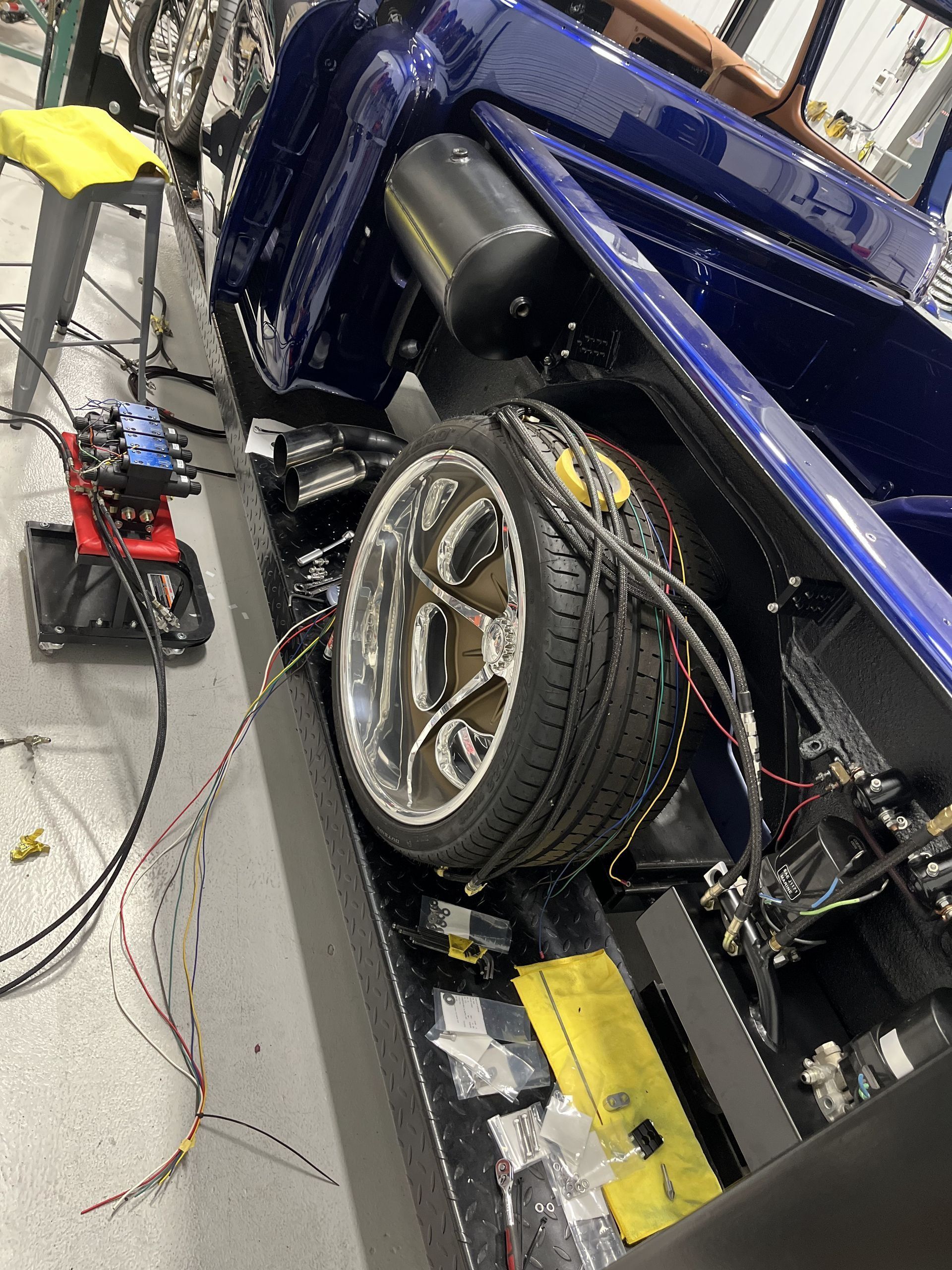Blue sports car on a shop floor, raised on equipment with a wheel removed and tools nearby