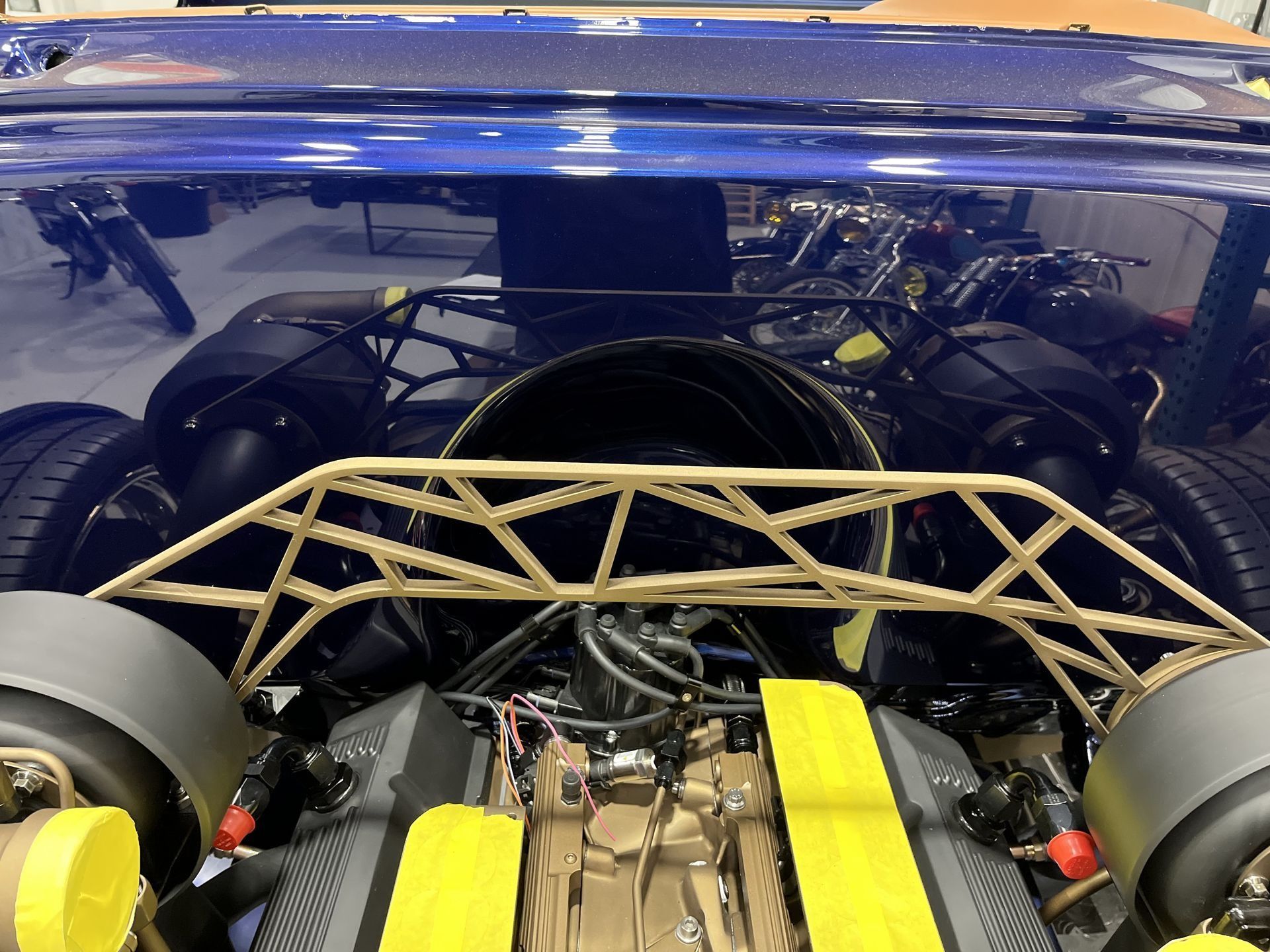 Blue race car rear with exposed engine, yellow straps, and roll cage under a blue body panel
