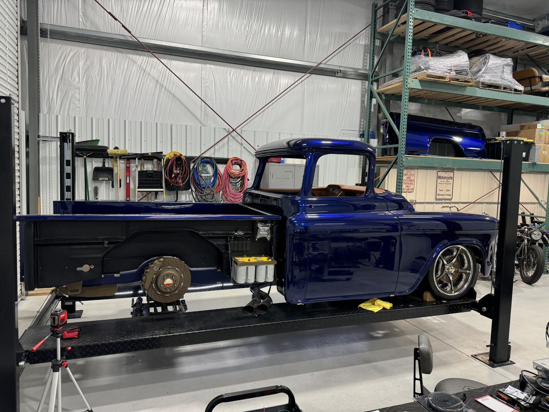 Blue classic pickup truck on a lift in a garage, with exposed rear wheel and polished front wheel.