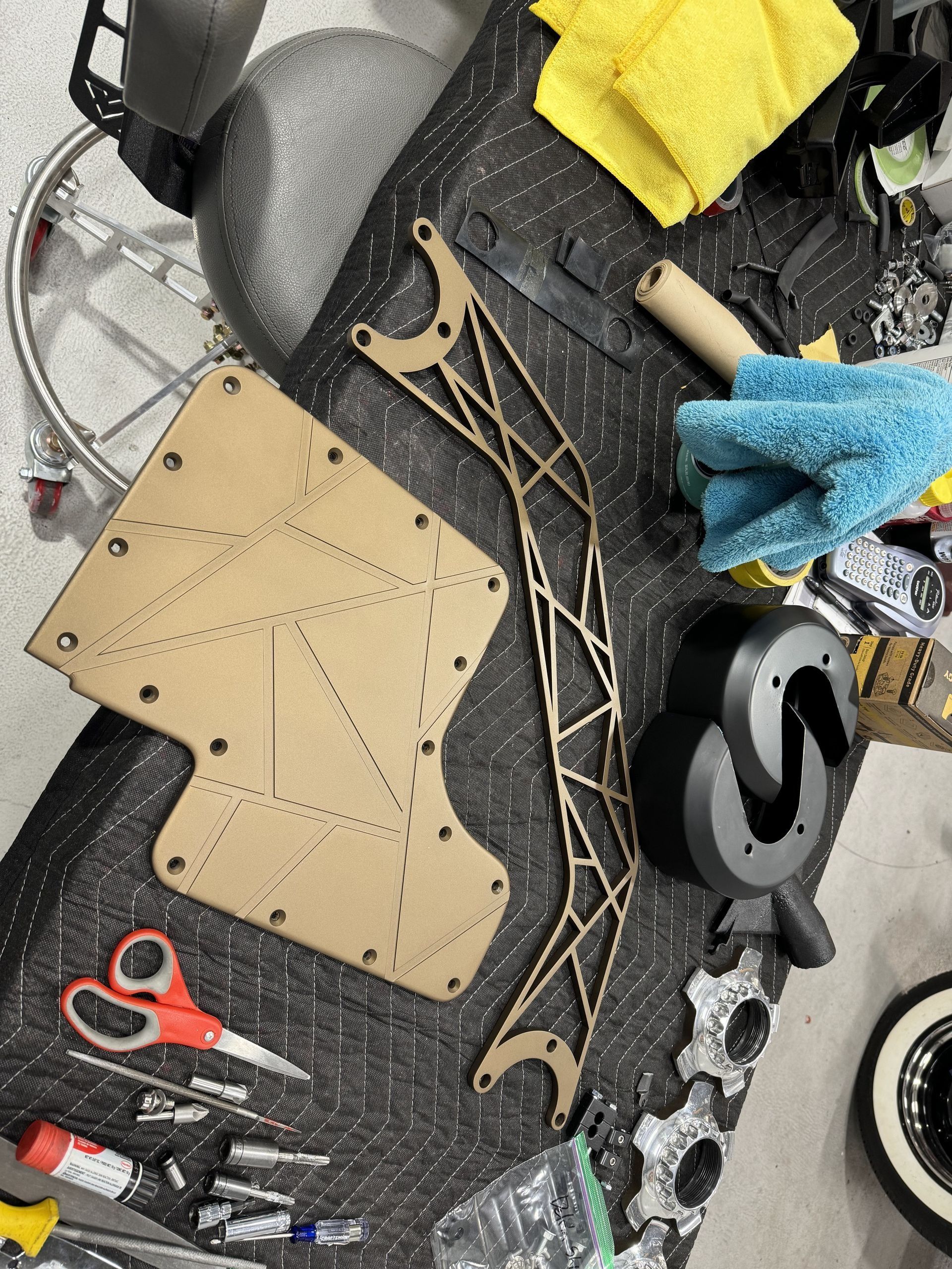 Workbench with tan leather pattern pieces, tools, scissors, and fabric on a black mat