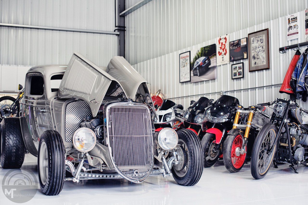 Classic silver hot rod in a garage with several motorcycles lined up behind it