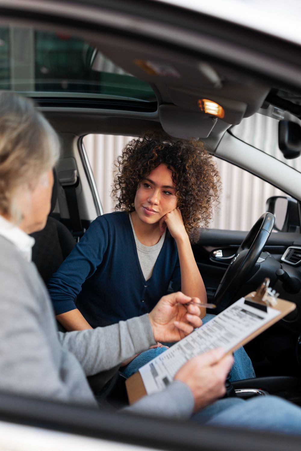 Instructor reviewing paperwork with a driver inside a car during a lesson