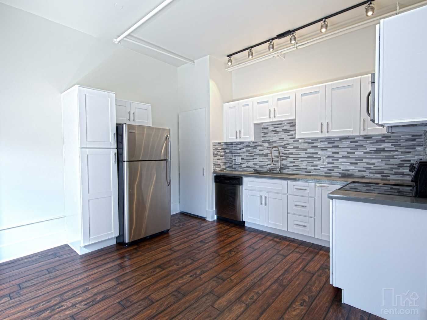 A kitchen with white cabinets , stainless steel appliances , and hardwood floors.