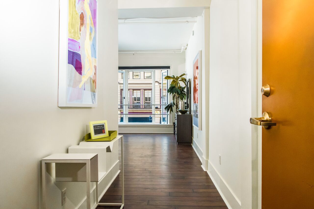 A long hallway with hardwood floors and a door leading to a living room.