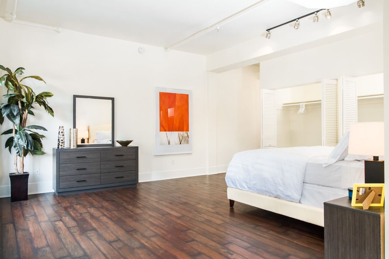 A bedroom with a bed , dresser , mirror and plant.