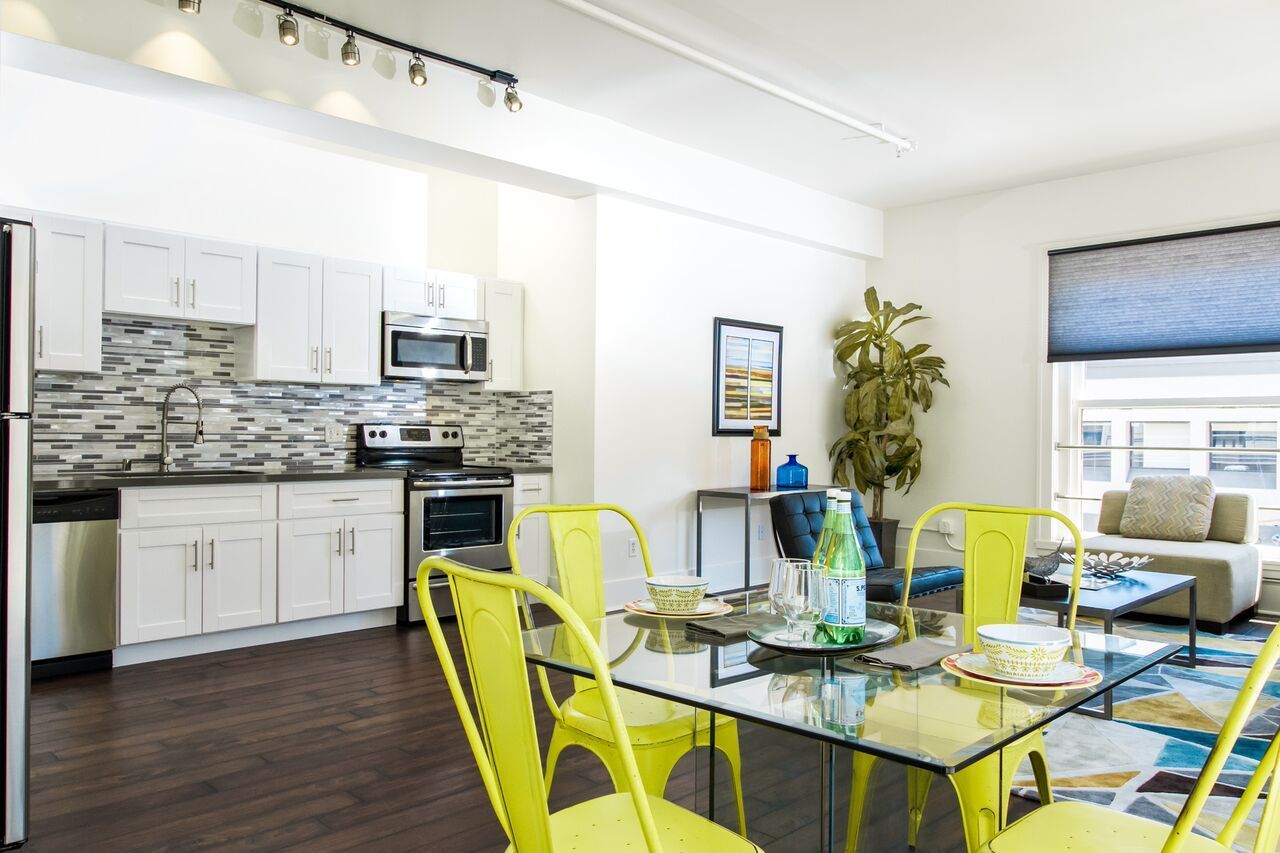 A kitchen and dining room with yellow chairs and a glass table.