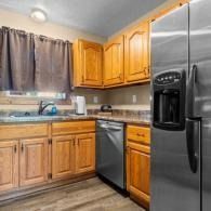 Modern kitchen with oak cabinets, stainless steel fridge and dishwasher, and a window over the sink.