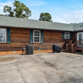 Wood-sided house exterior with driveway, porch steps, and two covered grills.