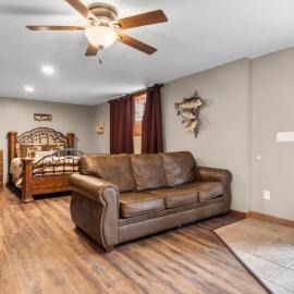 Spacious bedroom with leather sofa, wooden bed, ceiling fan, and hardwood floors.