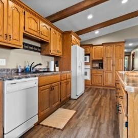 Bright kitchen with wood cabinets, white appliances, and a rustic ceiling with exposed beams.