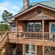 Wooden cabin exterior with porch, railing, stone chimney, and large windows