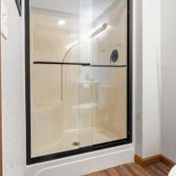 Walk-in shower with beige tile, black-framed glass door, and wood floor trim