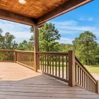 Wooden porch with railing overlooking green trees and blue sky