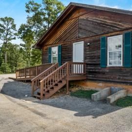 Rustic wooden cabin with a small porch and stairs, green shutters, in a wooded area