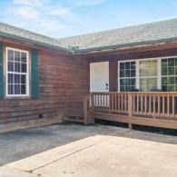 Wood-sided house exterior with front porch, white door, and concrete driveway