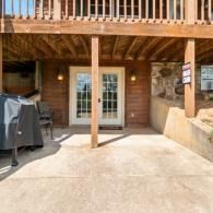 Covered backyard patio with double French doors, wooden deck above, and a grill on the left