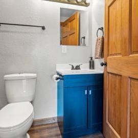 Small bathroom with white toilet, blue vanity sink, mirror, and wooden floor.