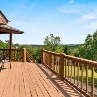 Wooden deck with railing overlooking a green landscape under a blue sky