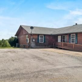 Rustic red wooden building with a ramp and a wide paved lot under a blue sky