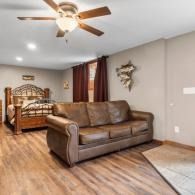 Bedroom with brown sofa, wooden bed, ceiling fan, and wood-look flooring in beige walls
