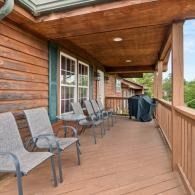 Wooden cabin porch with metal chairs and a grill, overlooking a scenic outdoor view