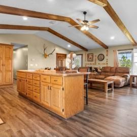 Spacious open-concept living room with wood beams, kitchen island, and tan sectional sofa