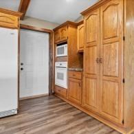 Kitchen with wood cabinets, white appliances, and a doorway with white trim and wood flooring