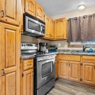 Compact kitchen with oak cabinets, stainless steel stove and microwave, and a window with brown curtains.