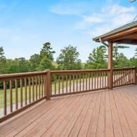 Wooden deck with railing overlooking a grassy landscape and trees under a blue sky