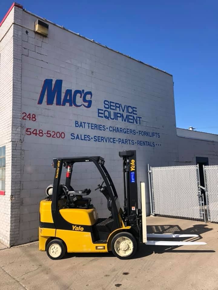 A yellow forklift is parked in front of a mac 's service equipment building.
